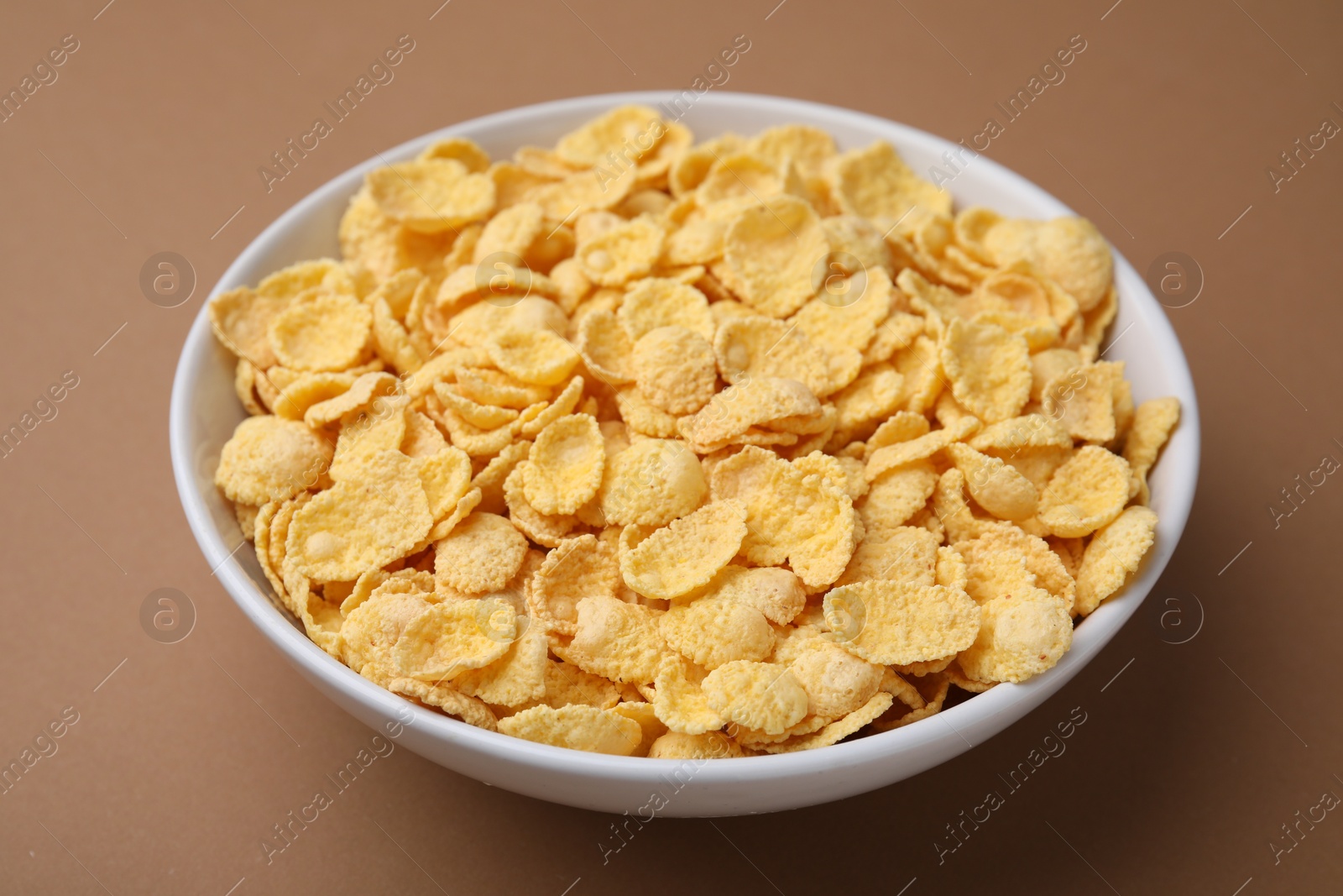 Photo of Breakfast cereal. Tasty corn flakes in bowl on brown table, closeup