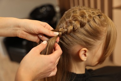 Photo of Professional hairdresser braiding girl's hair in beauty salon, closeup