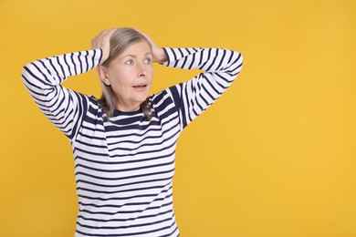 Portrait of surprised senior woman on yellow background, space for text