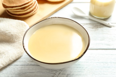 Photo of Bowl with condensed milk on wooden table. Dairy products