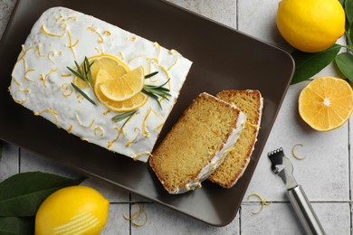 Photo of Tasty lemon cake with glaze, citrus fruits and zest grater on gray textured table, flat lay