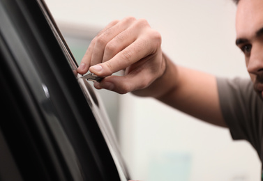 Photo of Worker tinting car window with foil in workshop, closeup