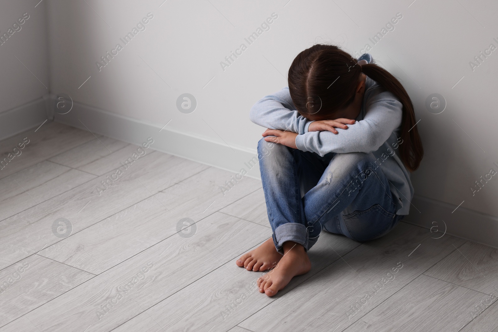 Photo of Child abuse. Upset little girl sitting on floor near light wall indoors, space for text