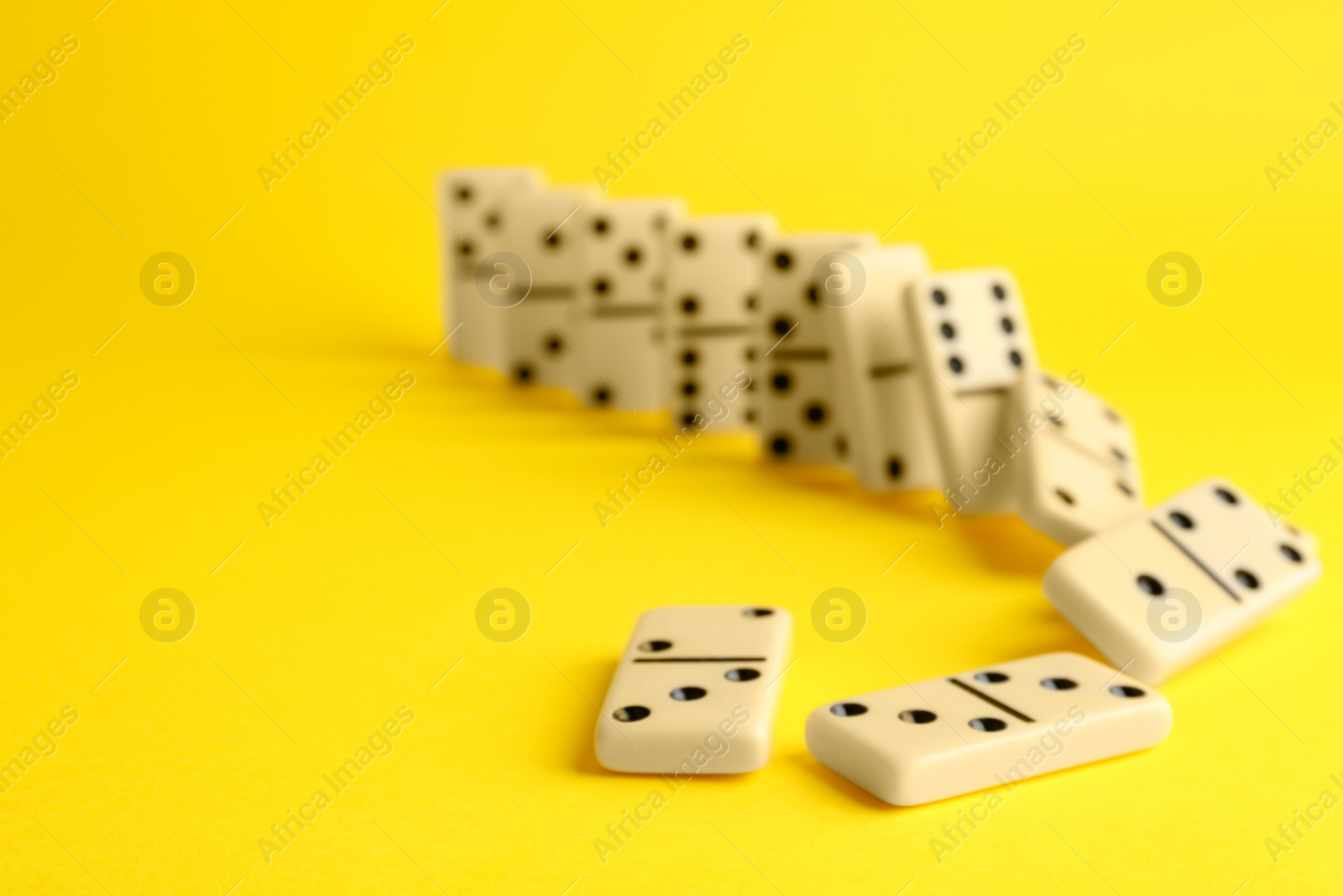 Photo of Falling white domino tiles on yellow background