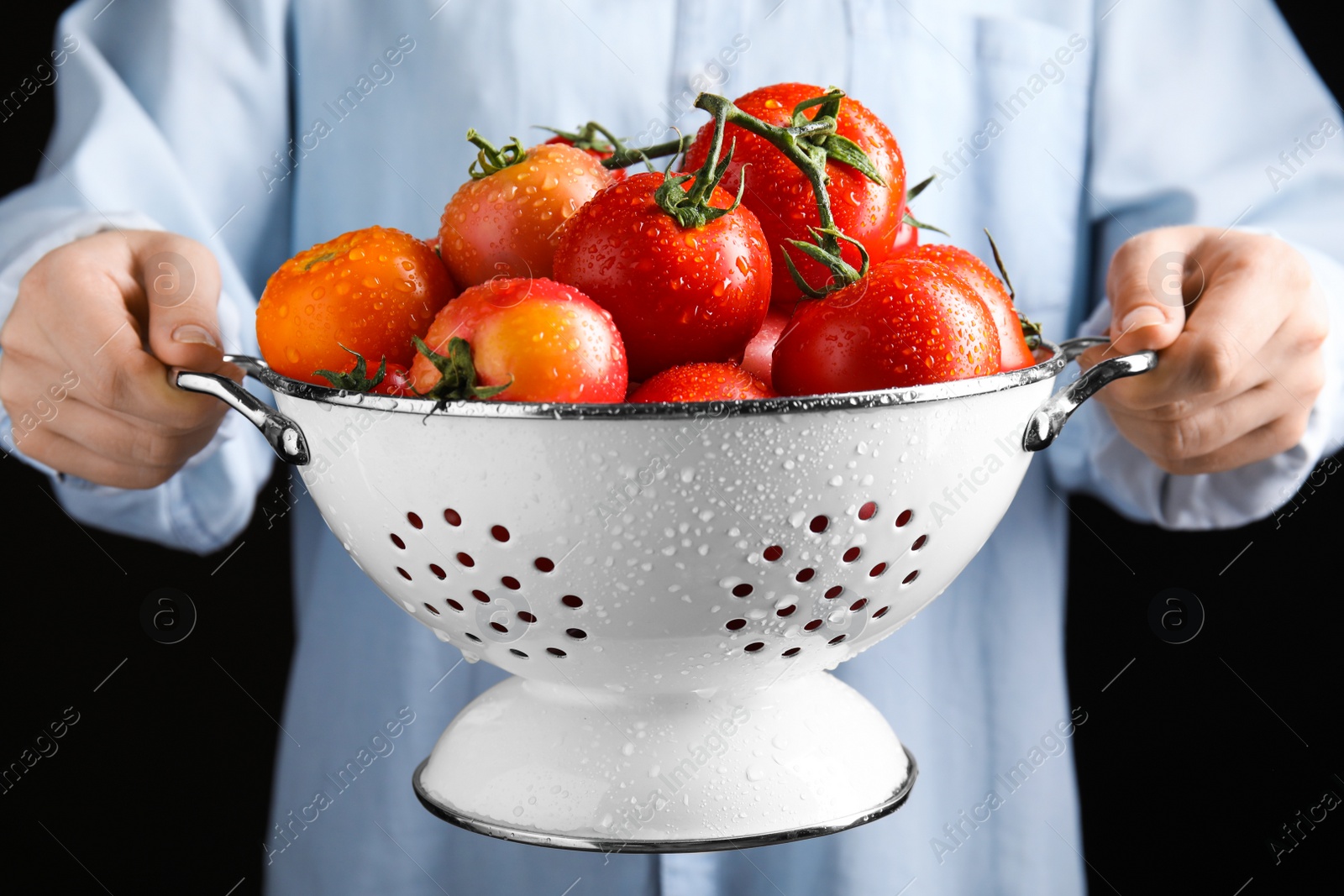 Photo of Woman holding colander with fresh ripe tomatoes on black background, closeup