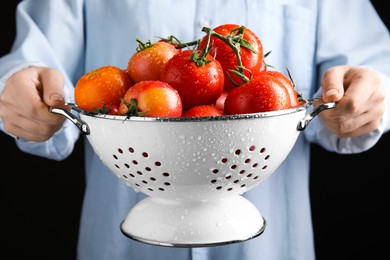 Photo of Woman holding colander with fresh ripe tomatoes on black background, closeup