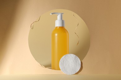Photo of Hole with face cleansing product and cotton pad on beige background