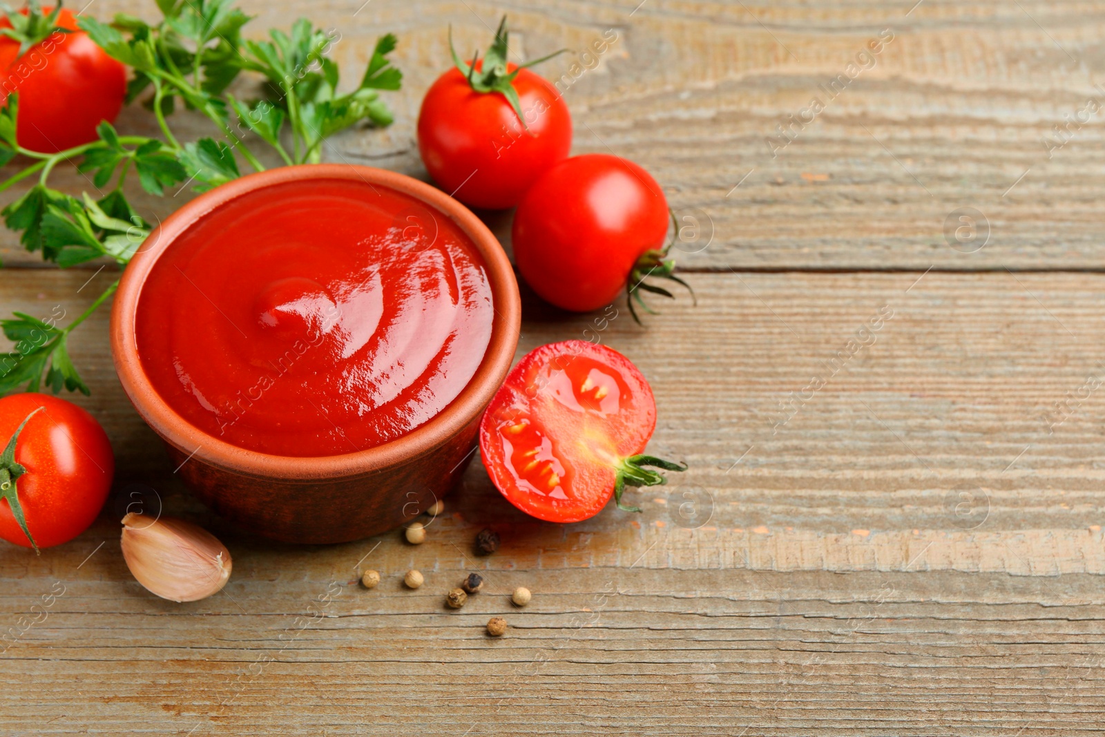 Photo of Tasty ketchup, fresh tomatoes, parsley and spices on wooden table. Space for text