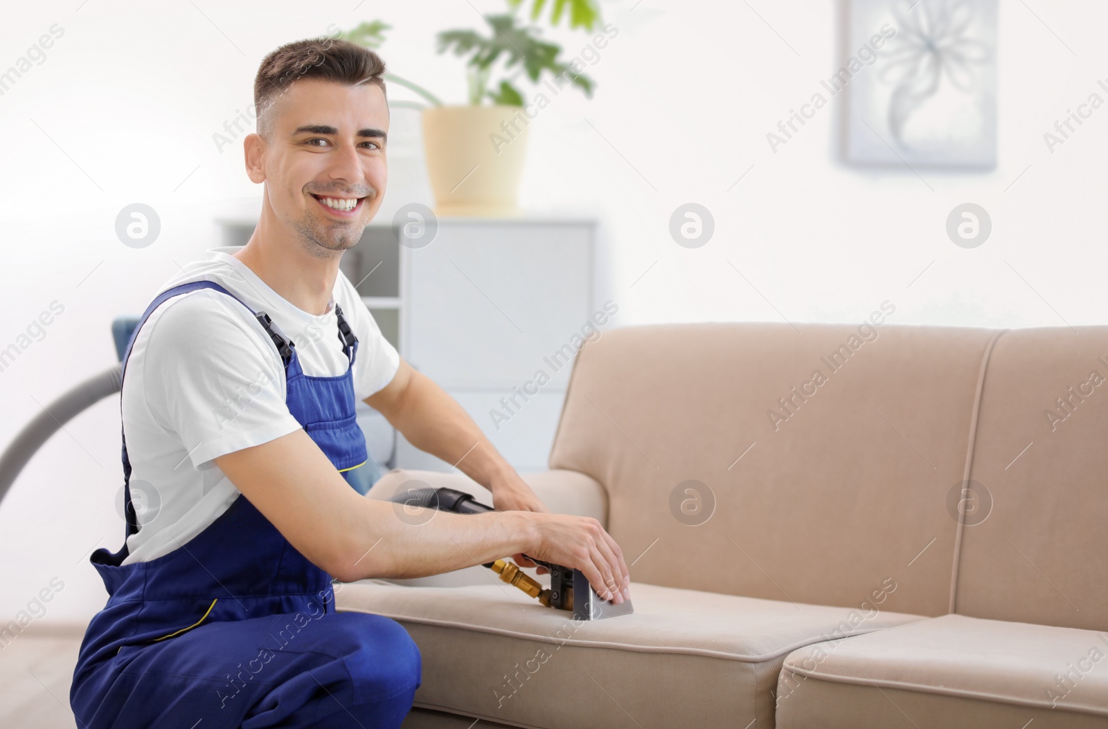 Photo of Dry cleaning worker removing dirt from sofa indoors