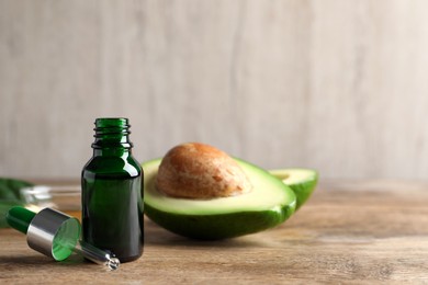 Photo of Bottle of essential oil, pipette and fresh avocado on wooden table, space for text