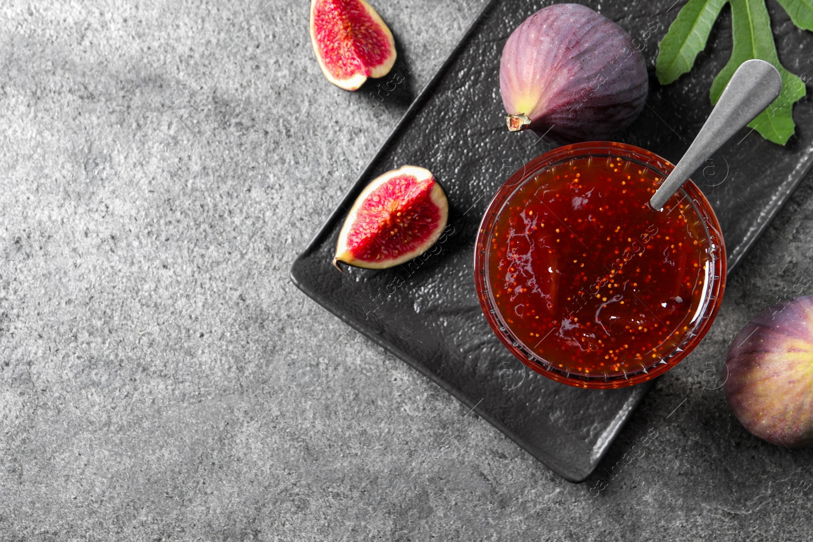 Photo of Glass bowl with tasty sweet jam and fresh figs on grey table, flat lay. Space for text