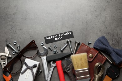 Photo of Card with phrase HAPPY FATHER'S DAY, different tools and male accessories on grey background, flat lay. Space for text