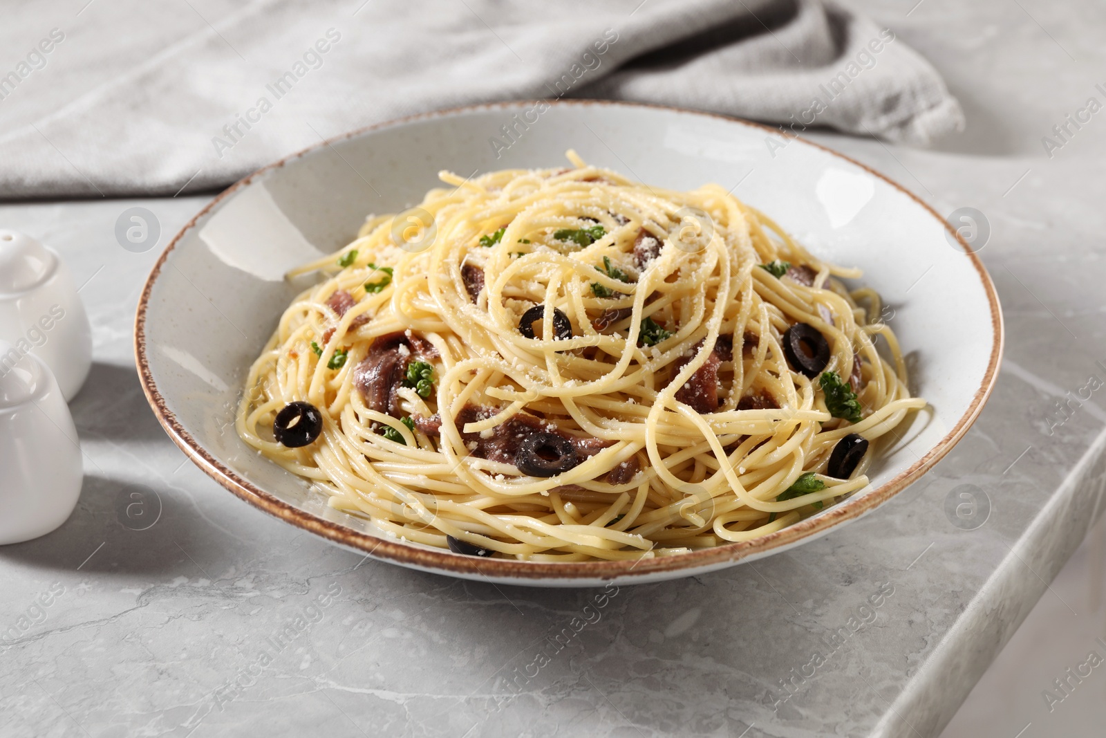 Photo of Delicious pasta with anchovies, olives and parmesan cheese served on grey marble table