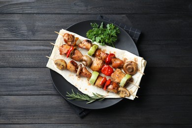 Photo of Delicious shish kebabs with vegetables and spices on black wooden table, top view