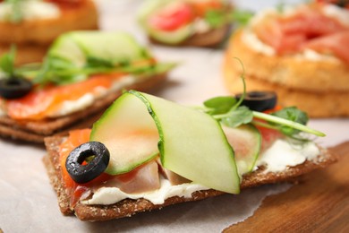 Photo of Tasty rye crispbreads with salmon, cream cheese and vegetables on wooden board. closeup