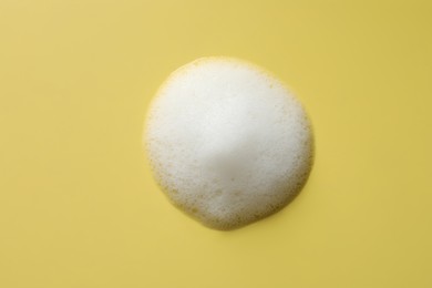 Photo of Drop of fluffy soap foam on yellow background, top view