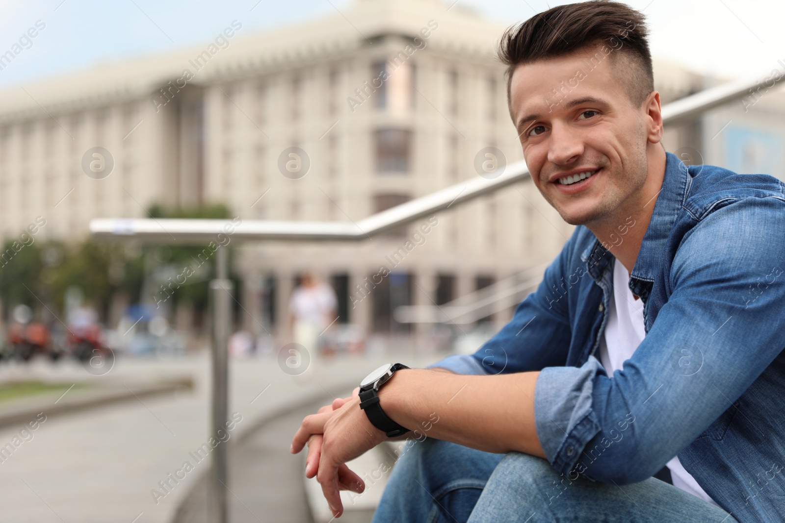 Photo of Portrait of handsome young man sitting on stairs outdoors. Space for text