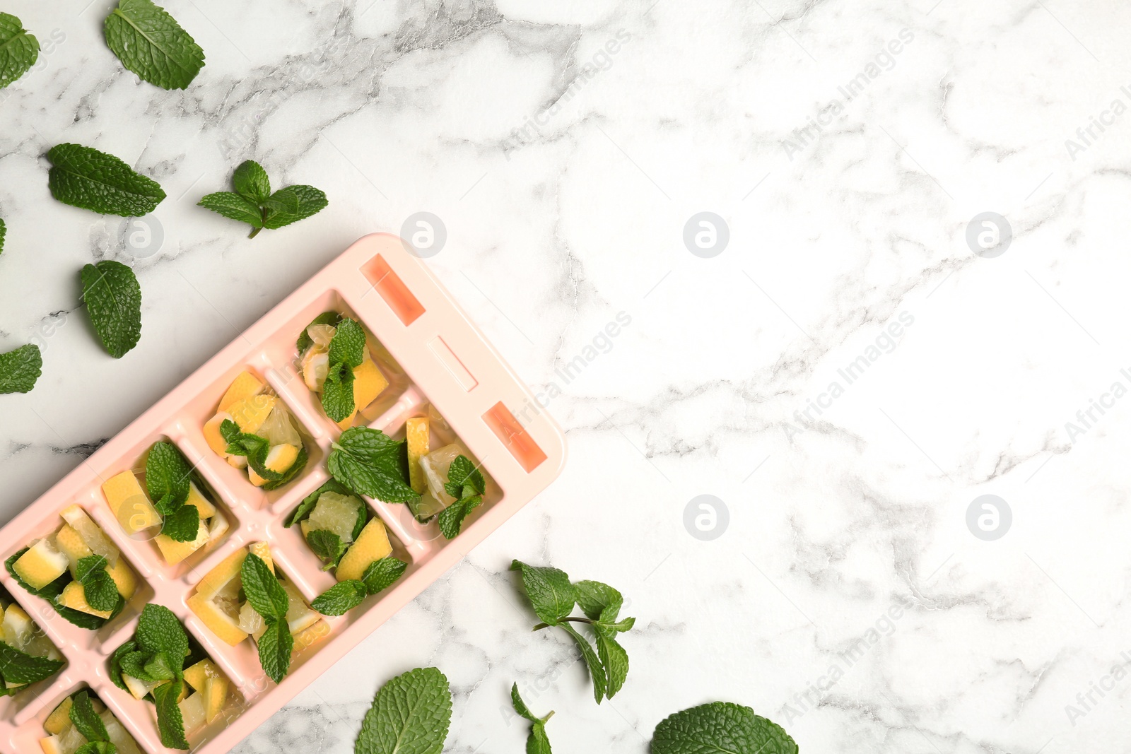 Photo of Ice cube tray with mint and lemon on marble background, top view. Space for text