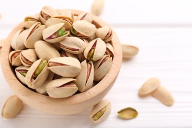 Photo of Tasty pistachios in bowl on white wooden table, closeup. Space for text