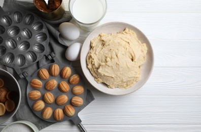 Delicious walnut shaped cookies with condensed milk and ingredients on white wooden table, flat lay. Space for text