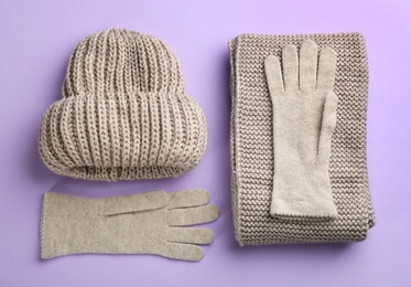 Photo of Stylish gloves, scarf and hat on violet background, flat lay