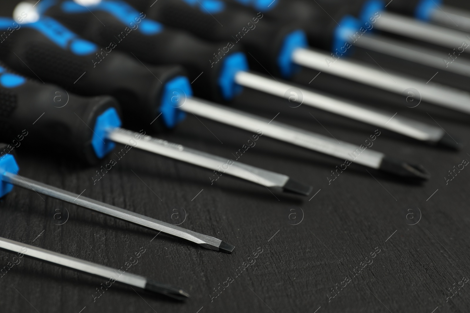 Photo of Set of screwdrivers on black wooden table, closeup