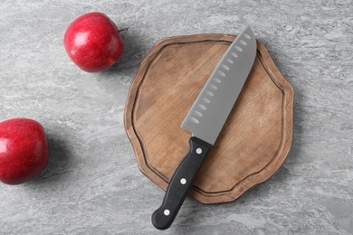 Cutting board with chef's knife and apples on grey background, flat lay