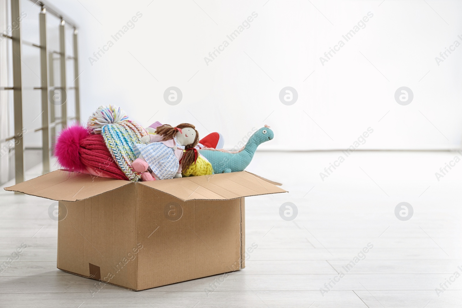 Photo of Donation box with clothes and toys on floor indoors. Space for text