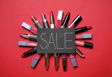 Many different lipsticks and card with word Sale on red background, flat lay