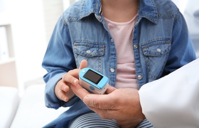 Doctor checking little girl's pulse with medical device in hospital, closeup