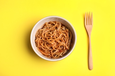 Cooked noodles and fork on yellow background, flat lay