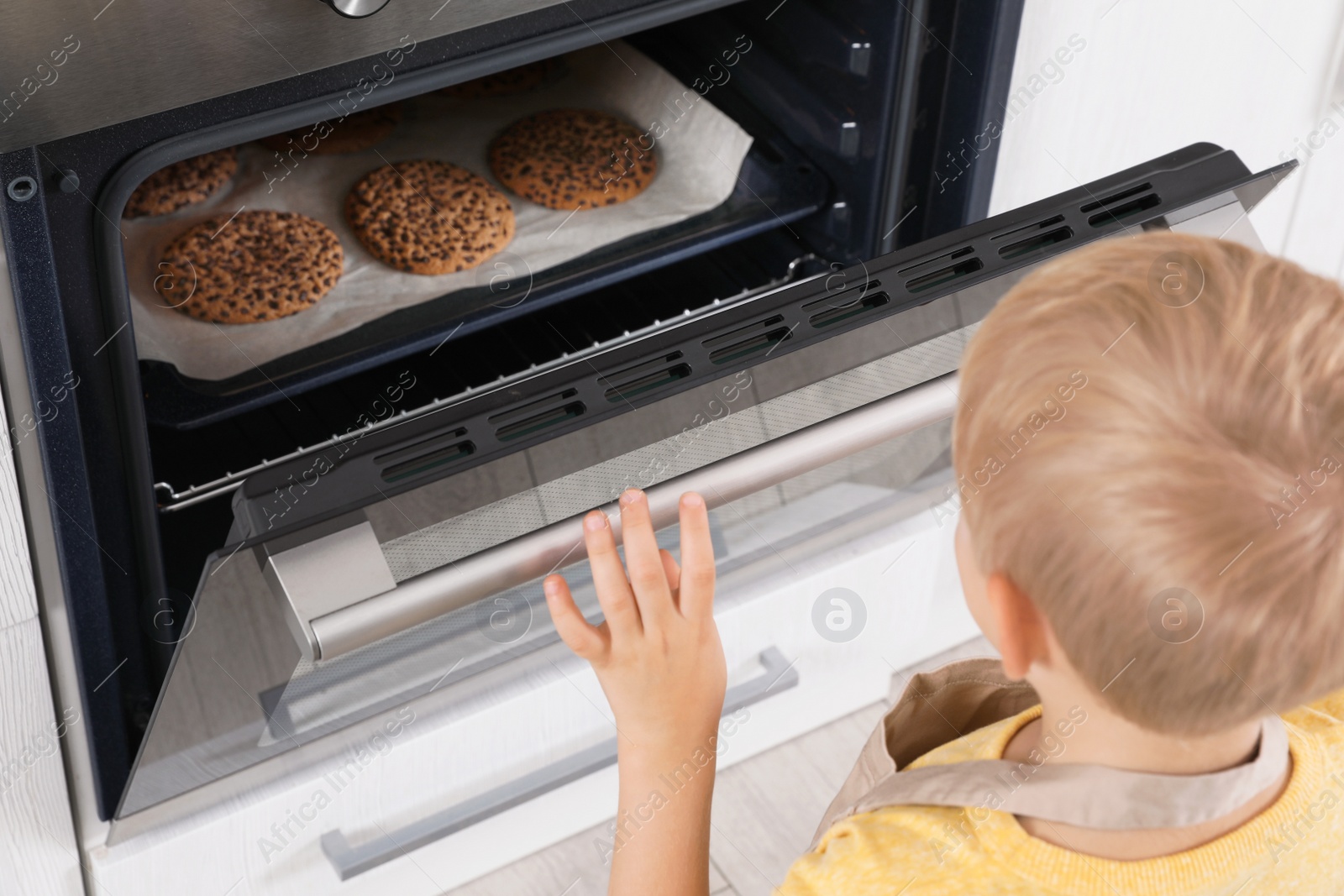 Photo of Little boy baking cookies in oven at home