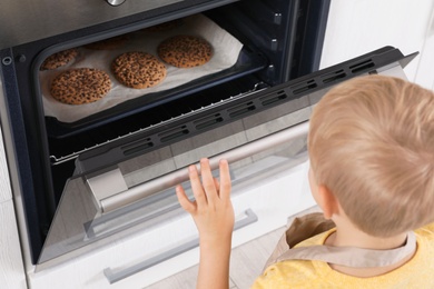 Photo of Little boy baking cookies in oven at home