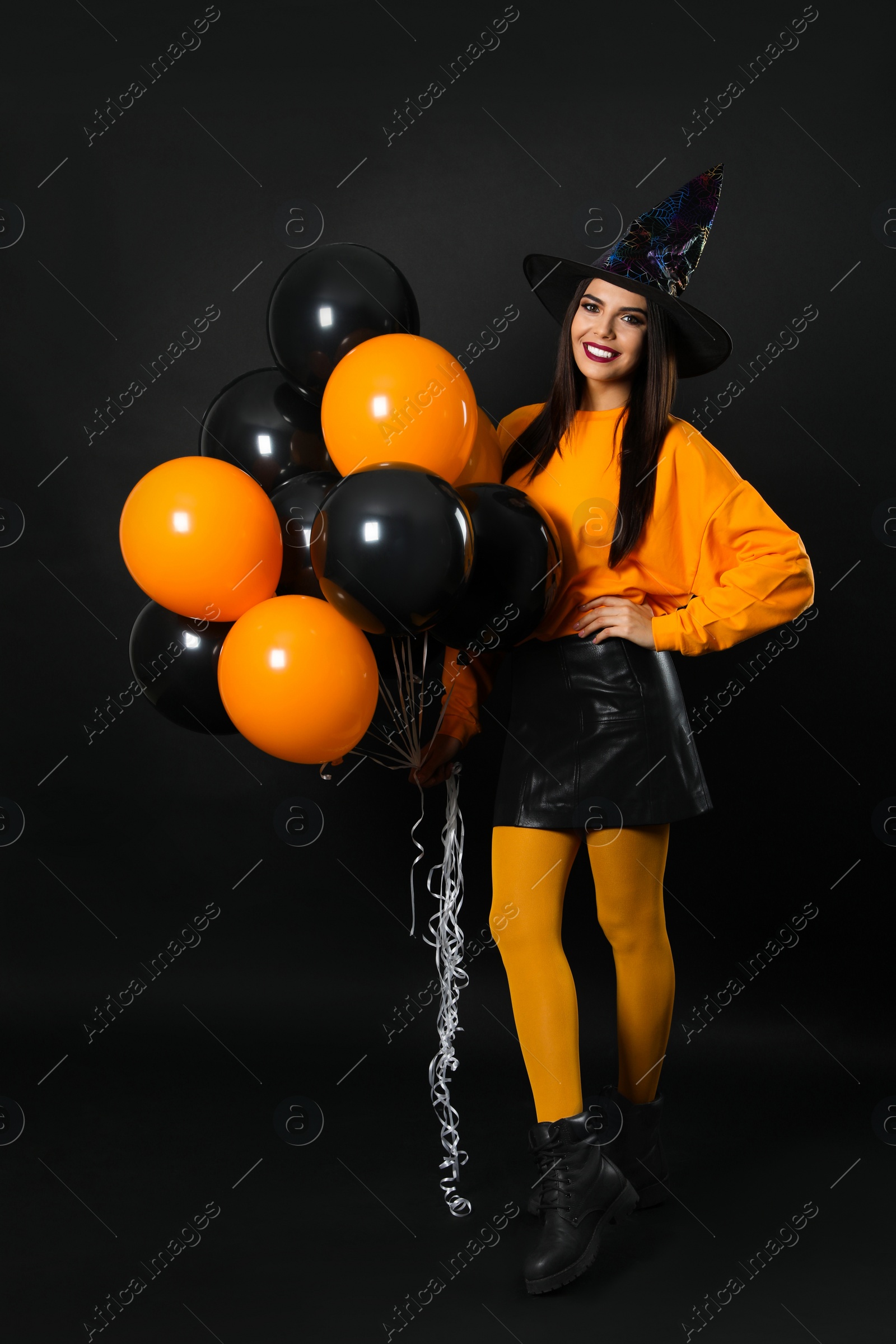 Photo of Beautiful woman wearing witch costume with balloons for Halloween party on black background