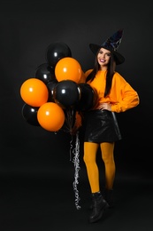 Photo of Beautiful woman wearing witch costume with balloons for Halloween party on black background