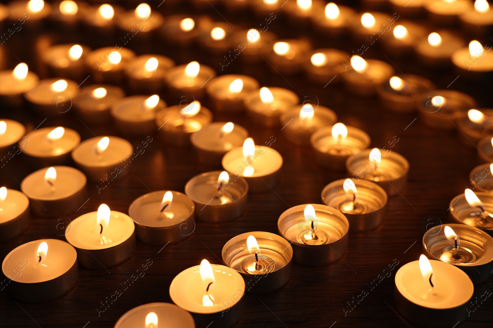 Photo of Burning candles on wooden table in darkness