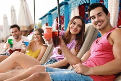 Happy young friends with fresh summer cocktails relaxing on sunbeds