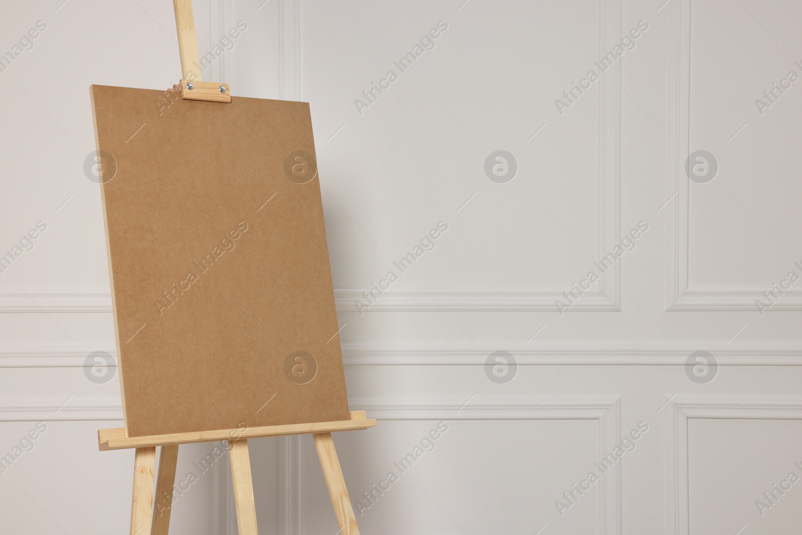Photo of Wooden easel with blank board near white wall. Space for text