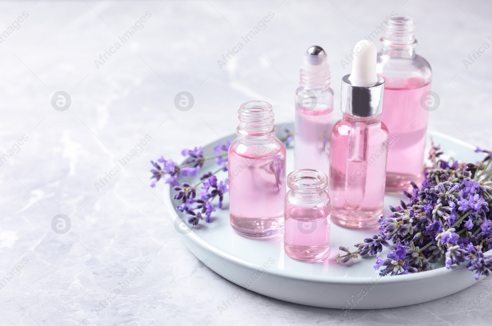 Photo of Tray with bottles of lavender essential oil and flowers on marble table. Space for text