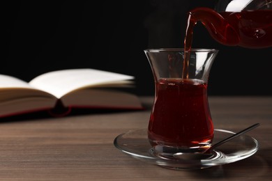 Pouring traditional Turkish tea from pot into glass on wooden table, space for text