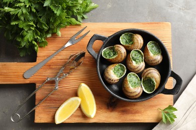 Photo of Delicious cooked snails in baking dish served on grey textured table, flat lay