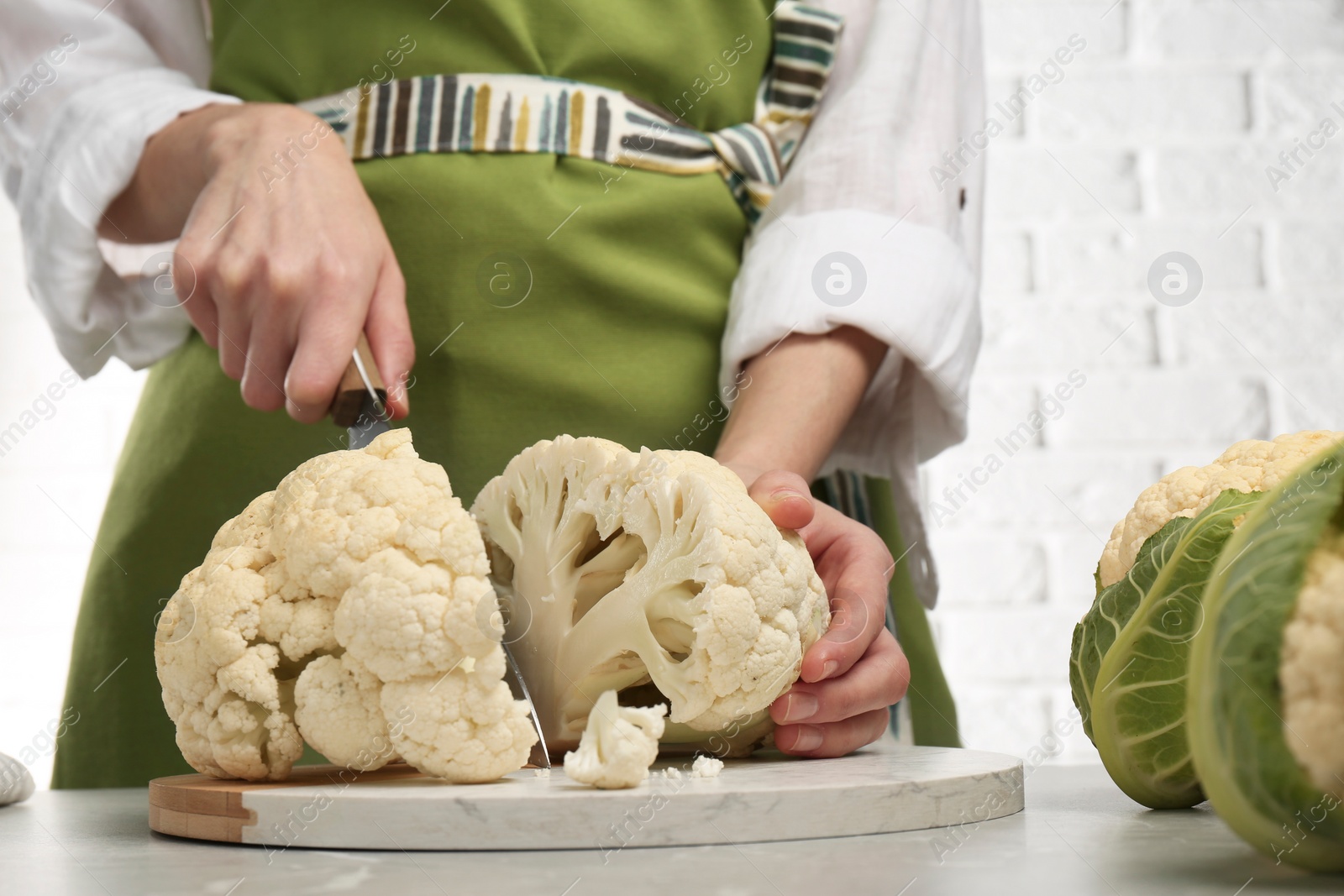 Photo of Woman cutting fresh cauliflower at light grey table, closeup