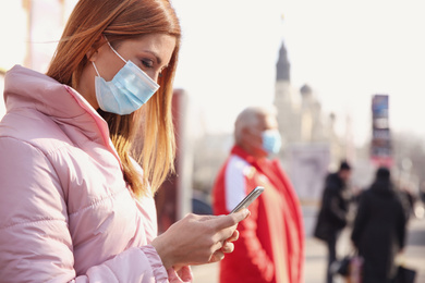 Photo of Woman with medical mask and mobile phone on city street. Virus protection
