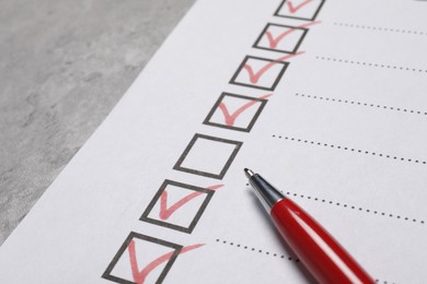 Paper sheet with checkboxes and pen on light grey table, closeup. Checklist