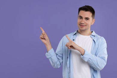 Photo of Special promotion. Young man pointing at something on violet background, space for text
