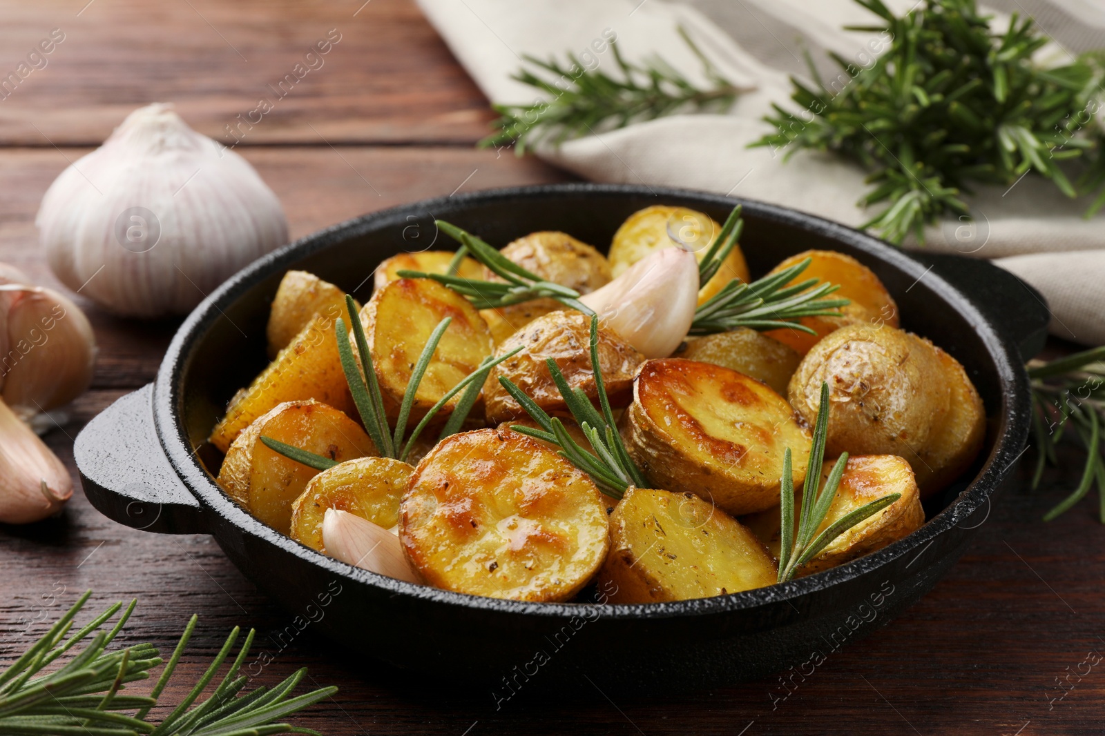 Photo of Delicious baked potatoes with rosemary in frying pan on table