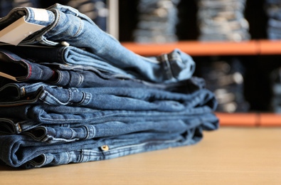 Photo of Stack of stylish jeans on display in shop, closeup