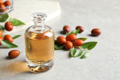 Jojoba oil in glass bottle and seeds on light grey table