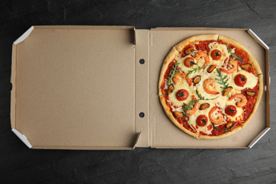 Photo of Delicious seafood pizza in cardboard box on black table, top view