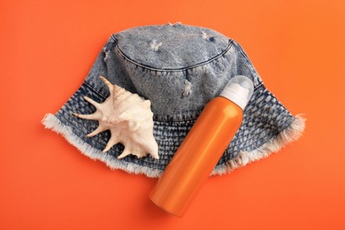 Photo of Bottle of sunscreen, seashell and denim hat on coral background, flat lay